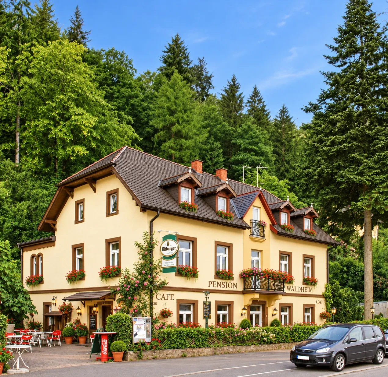 Das Hotel Waldheim in Freiburg-Günterstal: gelbes Haus mit Blumenkästen und Café-Terrasse direkt am Waldrand